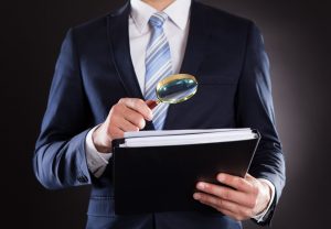 28162252 - midsection of businessman examining documents with magnifying glass against black background